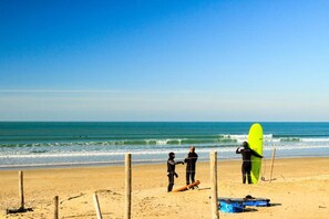 A beach with a wooden fence, a surfboard, and a person standing by the water.