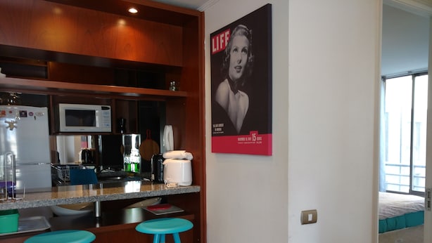 Eine kompakte Küche mit Mikrowelle, Kaffeemaschine und Barhocker. An der Wand hängt ein LIFE Magazin-Poster.