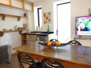 A kitchen with a wooden table, chairs, a stove, and a television displaying a news program. - Apartamento Living Lecannelier (Santiago)