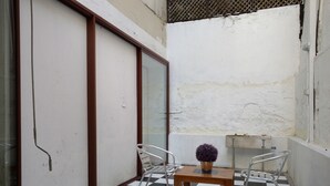 Ein kleiner, abgeschlossener Balkon mit kariertem Boden, einem Holztisch mit einem Blumentopf und Metallstühlen.