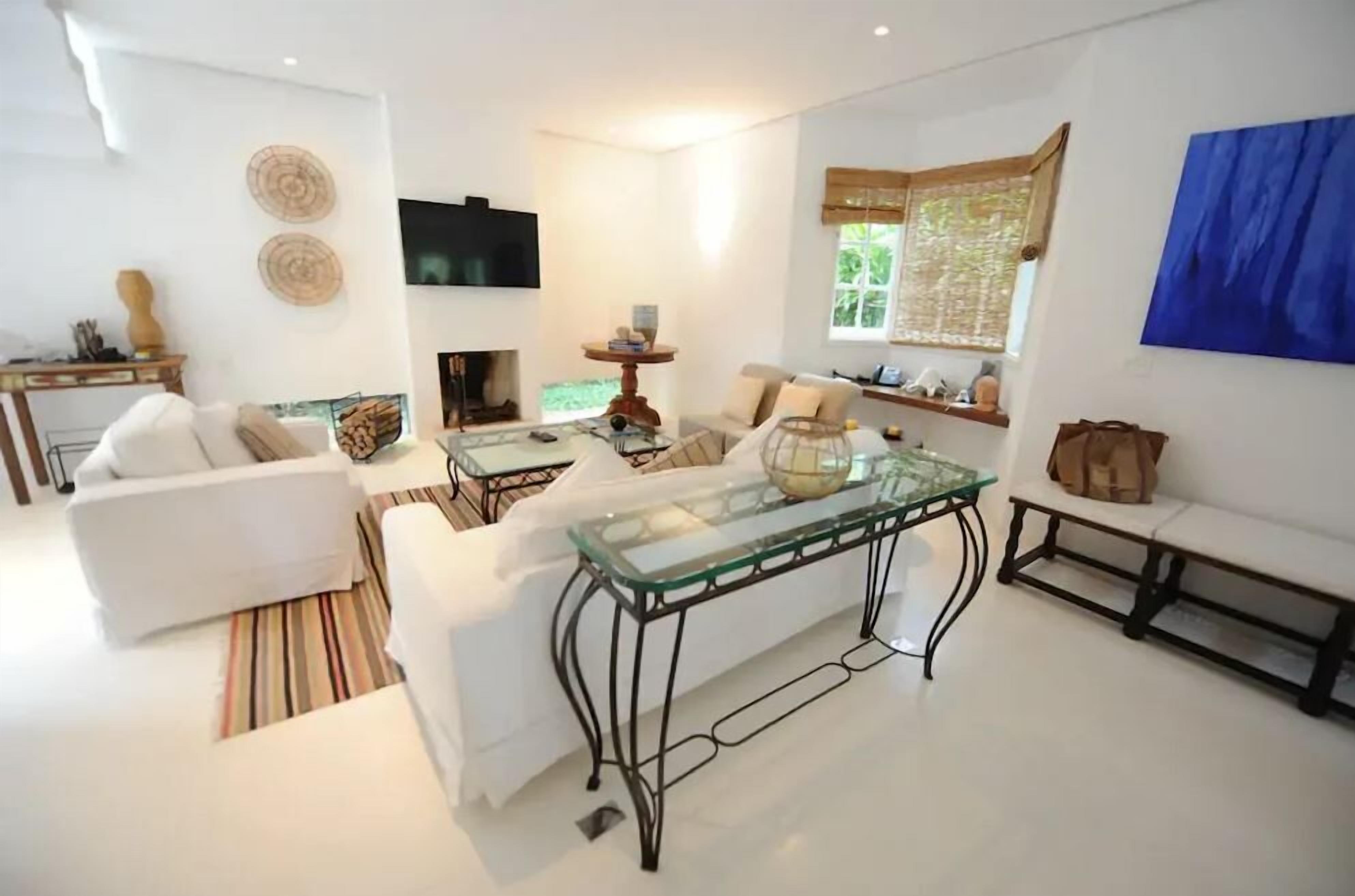 A modern living room with a white sofa, a glass coffee table, a fireplace, and a television.