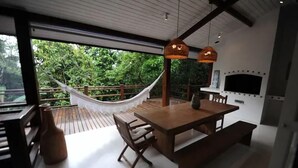 An outdoor dining area with a wooden table and benches, a hammock, and a TV mounted on the wall.