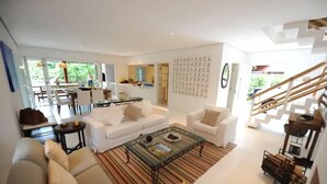A modern living room with white sofas, a glass coffee table, and a staircase.