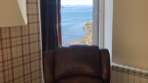A room with a view of the sea, a brown leather chair, plaid curtains, and a radiator. - The Millcroft Hotel (Gairloch)