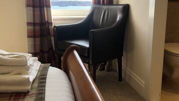 Hotellihuone, jossa on sänky, tuoli ja näkymä rannalle.