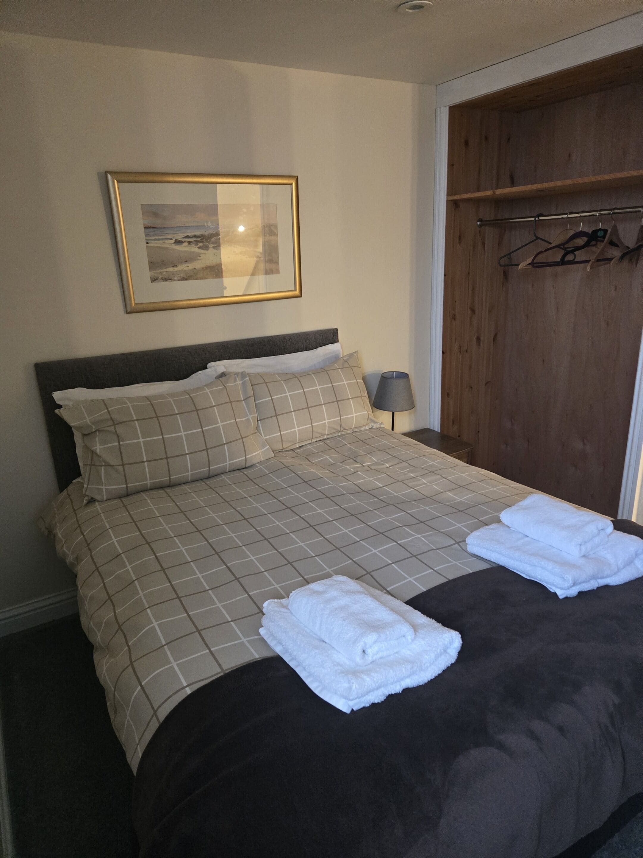 A neatly made bed with a checkered bedspread, two pillows, and two folded towels on the bed.