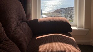 A room with a view of the sea through a window, a brown sofa, and a lamp. - The Millcroft Hotel (Gairloch)