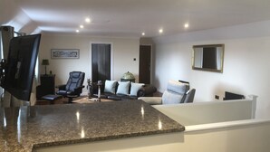 A living room with a dark brown leather sofa, a white armchair, a coffee table, and a television. - The Millcroft Hotel (Gairloch)