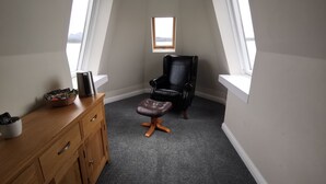 A room with a high ceiling, a black leather chair, a wooden cabinet, and a small stool. - The Millcroft Hotel (Gairloch)