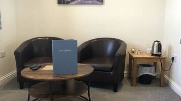 A room with two leather sofas, a small wooden table, a coffee maker, and a painting on the wall.