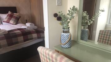 Un dormitorio ordenado con cama, una mesita de noche con un florero, una silla y un espejo.
