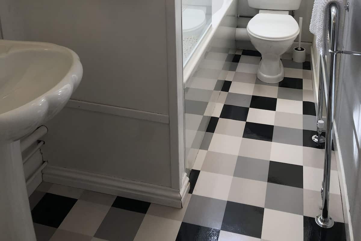 Kylpyhuone, jossa on ruutukuviollinen lattia, wc-istuin, pesuallas ja suihku.