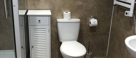 A bathroom with a toilet, a small cabinet, a glass shower enclosure, and a sink.