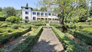 Een groot, wit gebouw met een symmetrische tuin met keurig bijgesnoeide hagen en een grindpad.