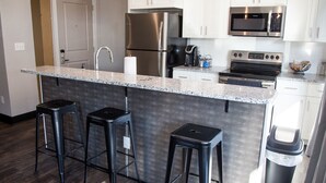 A modern kitchen with a granite countertop, stainless steel appliances, and black bar stools. - Gibson's Warehouse (Staunton)