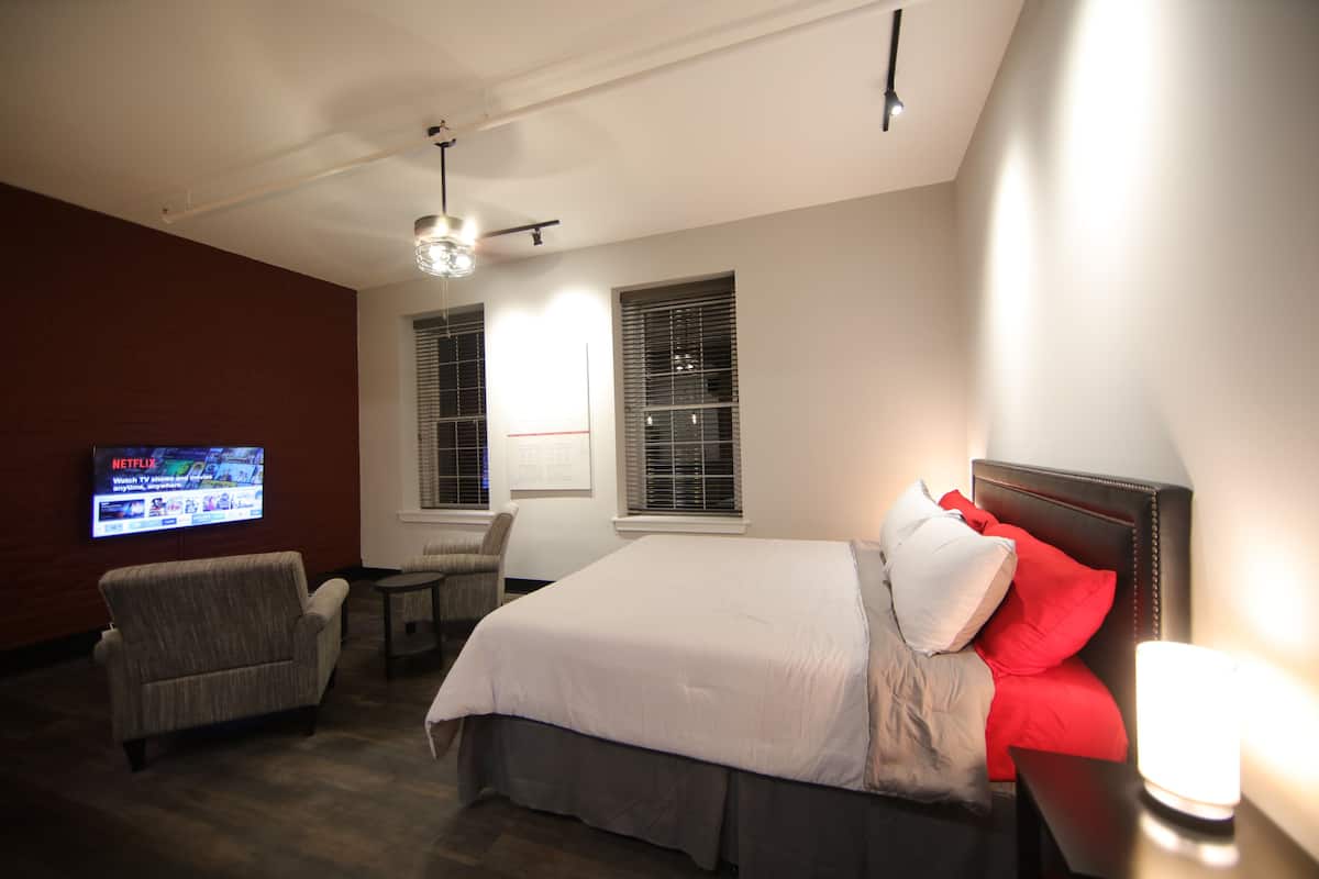 A hotel room with a bed, a chair, a TV, and a window with blinds.