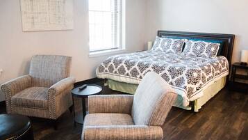 A bedroom with a bed, two armchairs, a small table, and a window with blinds.
