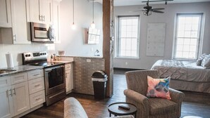 A spacious living area with a sofa, armchair, and ottoman, a kitchen with modern appliances, and a large window providing natural light. - Gibson's Warehouse (Staunton)