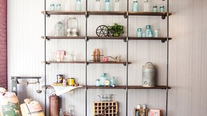 A rustic metal shelving unit with various vintage items, including glass jars, metal containers, and a wooden crate. - Gibson's Warehouse (Staunton)