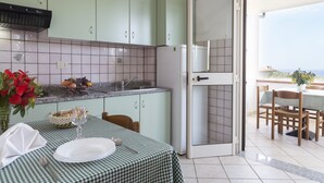 Una cocina con gabinetes verdes, un refrigerador blanco y un comedor con una mesa dispuesta para dos.