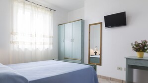Un dormitorio con cama, armario, televisor, espejo y escritorio con planta en maceta.