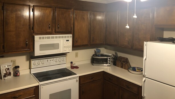 A kitchen with wooden cabinets, a white stove, a microwave, a toaster, and a refrigerator.