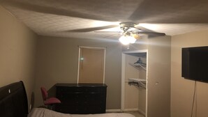 A bedroom with a bed, a dresser, a desk, a chair, a ceiling fan, a TV, and a closet.