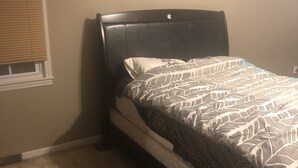 A single bed with a headboard, a window with blinds, and a carpeted floor.