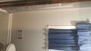 A bathroom with a toilet, a vent, and a window with blue curtains.