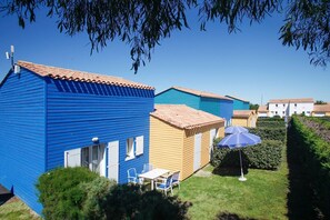Une rangée de maisons de vacances aux couleurs vives, chacune dotée d’un petit patio et d’une table avec des chaises.