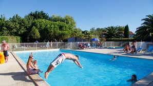 Uma piscina cercada por pessoas, com uma área delimitada e árvores ao fundo.