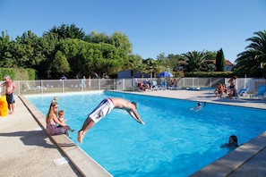 Ein Pool mit Personen in der Nähe, einem umzäunten Bereich und Bäumen im Hintergrund.