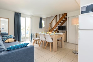 Ein modernes Wohnzimmer mit einer Couch, einem Esstisch mit Stühlen, einer Treppe und einem Fernseher.