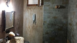 A bathroom with a stone wall, a wooden door, a towel hanging, and a window. - Hostal Boutique (Tulum)