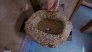 A stone mortar with a pestle, a shell, and a metal object on a blue floor. - Hostal Boutique (Tulum)