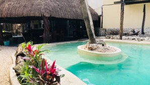A swimming pool with a circular island, surrounded by tropical plants and a thatched-roof structure. - Hostal Boutique (Tulum)