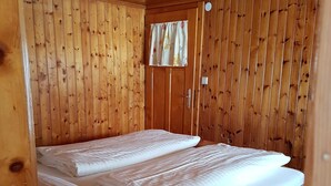 A wooden cabin room with a bed, a window with curtains, and a door. - Vacation apartment Helma - Holiday apartment 1 (Blons)