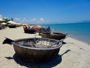 Several traditional boats on a sandy beach with a clear blue sky and calm sea in the background.