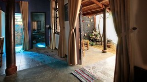 Habitación con techo de madera, suelo estampado y vista a un espacio exterior con pared de ladrillo y árboles.