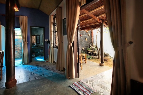 A room with a wooden ceiling, patterned floor, and a view of an outdoor area with a brick wall and trees.