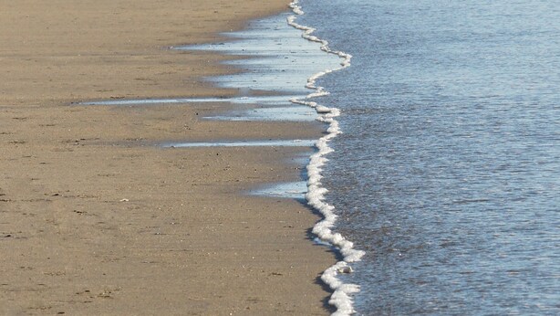 Une plage où l’on distingue clairement la limite entre le sable mouillé et le sable sec, ce qui indique le niveau de la marée.