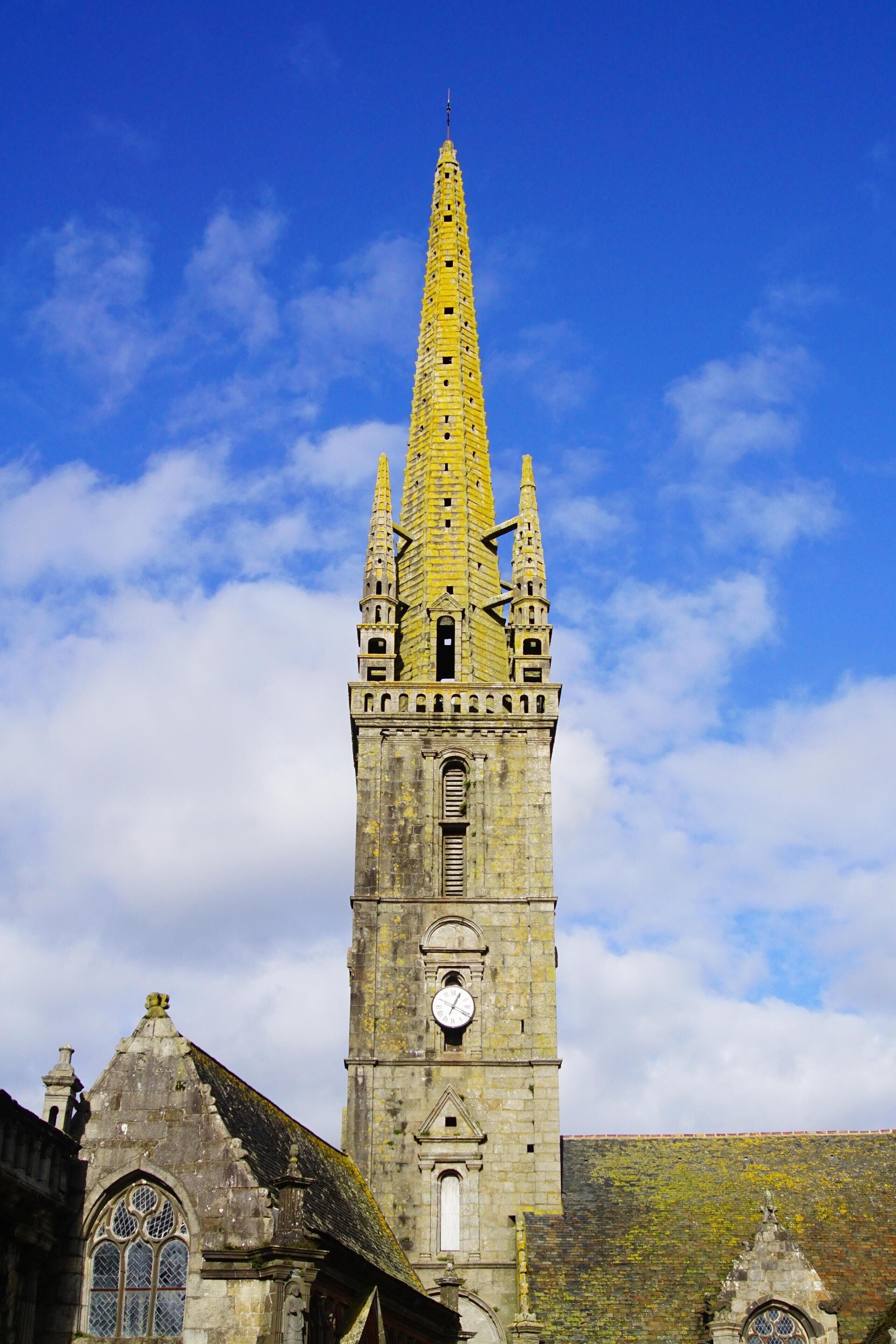 A historic church tower with a clock, pointed spire, and arched windows.
