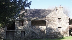 Un bâtiment en pierre avec un toit à forte pente, une porte en bois et une petite fenêtre.