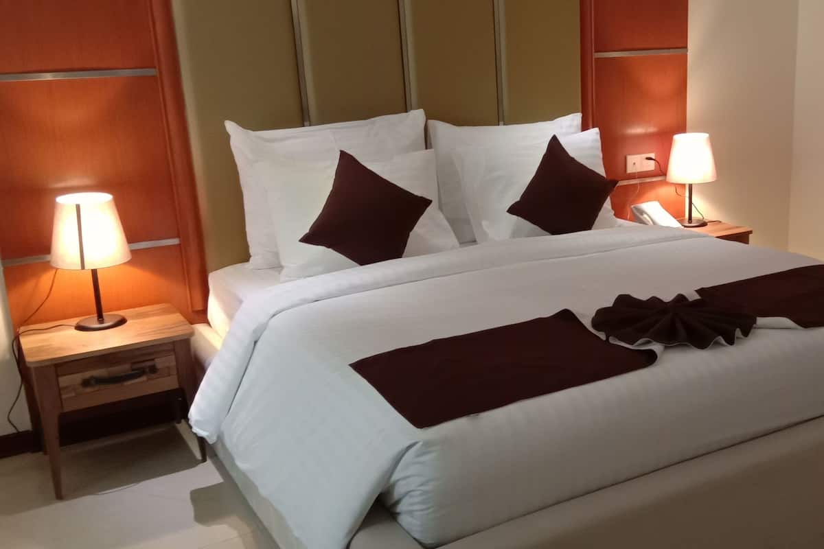 Una camera d'albergo con un letto grande, due comodini, un tavolino, una lampada su ciascun tavolo e un telefono sul tavolino.