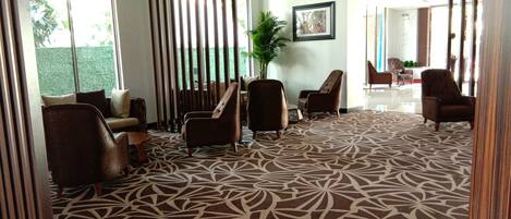 Un vestíbulo con alfombra estampada, varias zonas de estar y una planta grande.