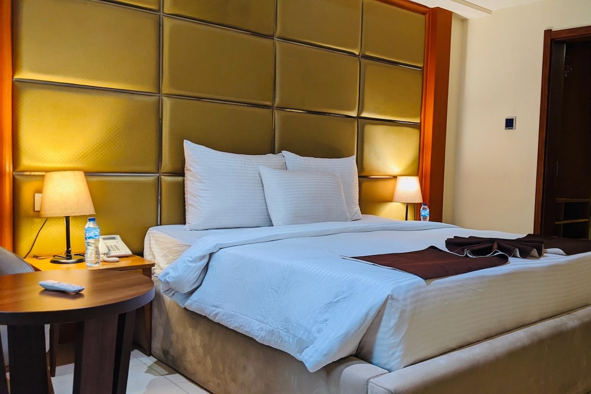 Een hotelkamer met een groot bed, een nachtkastje met lamp, een telefoon en een waterfles.