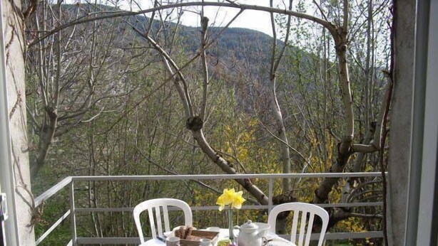 Mesa para dos con sillas y mantel blanco, con vista a una ladera boscosa.