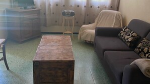 Una sala de estar con una mesa de centro de madera, un sofá, una silla y un televisor sobre un mueble de madera.