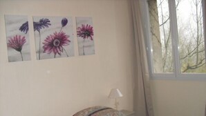 Un dormitorio con cama, arte floral en la pared, una ventana y una lámpara.