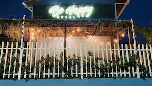 Un hotel con un letrero de neón que dice "Be Aimee HOTEL" y una cerca blanca de piquetes al frente.